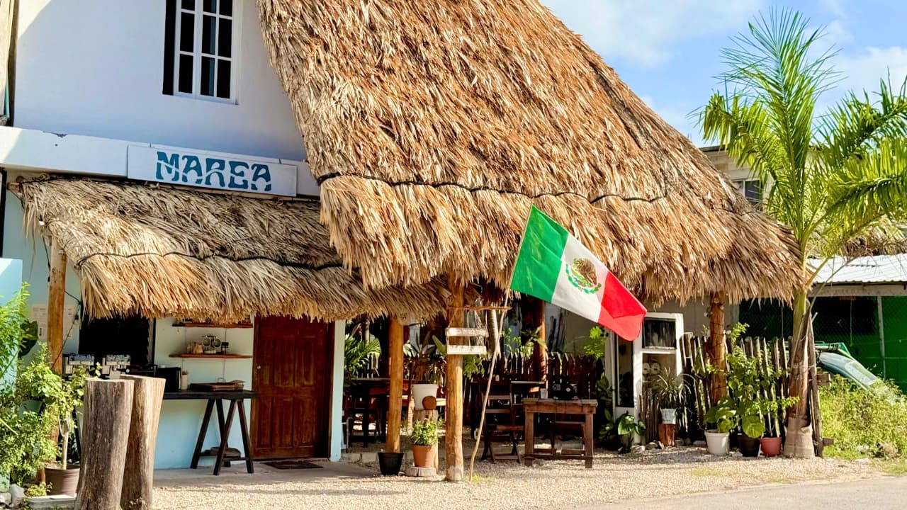 Fachada de Marea Brunch & Coffee en Mahahual: palapa de guano, letrero con el nombre del café y bandera de México
