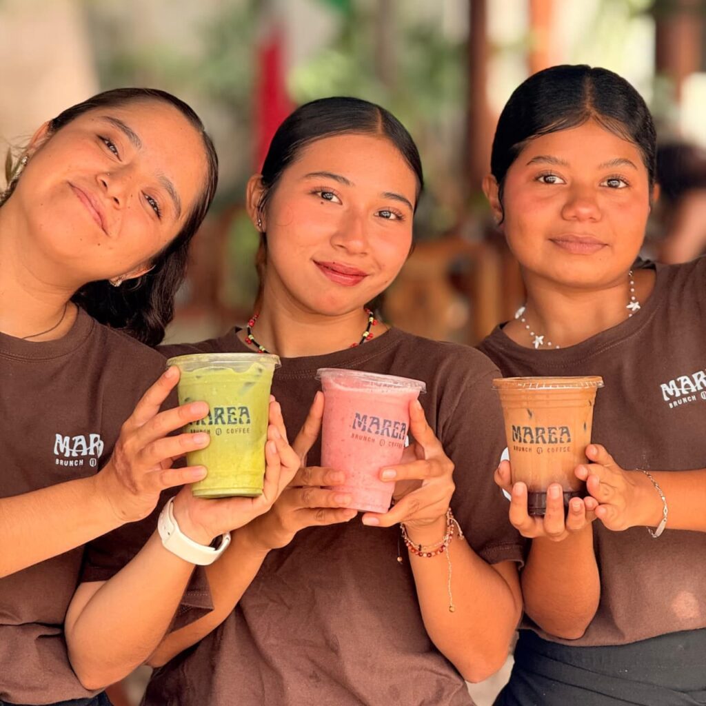 Tres integrantes del equipo de Marea, con playera café de la casa, sosteniendo un matcha, un smoothie de fresa y un latte frío